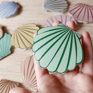 Könnte beinhalten: Eine grüne Muschel mit weißen Linien, ein beliebtes Dekorationsobjekt für Strand-Dekorationen.