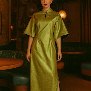 以下が含まれることがあります： 短いワイドスリーブとハイカラーのオリーブグリーンのロングドレス。ドレスはサイドにスリットがあり、ネックラインには小さなキーホールディテールがあります。ドレスは光沢のあるテクスチャード加工の生地で作られています。