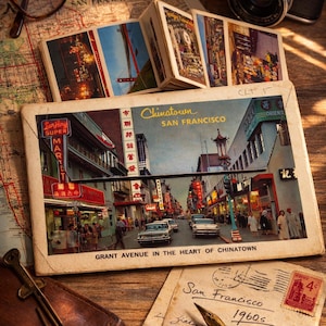 Puede incluir: Naturaleza muerta de temática viajera con una postal de Chinatown, San Francisco, de los años 60. La imagen incluye una cámara, gafas, un mapa y una cartera de cuero, evocando la exploración y la nostalgia.