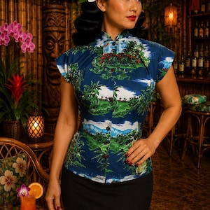 May include: A short-sleeved, button-down blouse in a deep blue hue, featuring a repeating tropical landscape print with green palm trees, lush foliage, and white clouds. The garment has a high mandarin collar and a fitted silhouette.