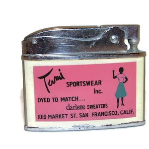 May include: Vintage chrome and cream-colored lighter with a pink label. The label features the text "Tami Sportswear Inc." and a silhouette of a woman. The lighter has a flip-top design.