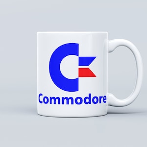 May include: White ceramic mug with a blue and red Commodore logo and the word "Commodore" printed in blue below the logo.
