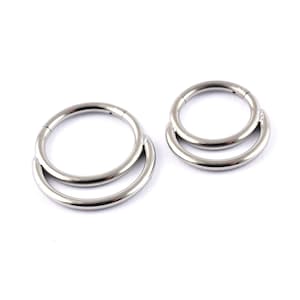 May include: Two silver double hoop earrings. The hoops are made of two circles, one slightly larger than the other, with the smaller circle sitting inside the larger circle.