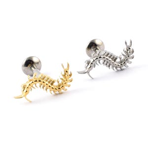 May include: Two stud earrings featuring a centipede design. One is gold-coloured, the other silver-coloured. Each earring has a post and a round back. The centipede design is detailed and curved.