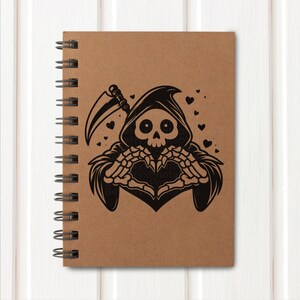 May include: A brown spiral bound notebook with a black illustration of the Grim Reaper making a heart shape with its skeletal hands. The Reaper is wearing a hooded robe and holding a scythe. There are small hearts scattered around the Reaper.