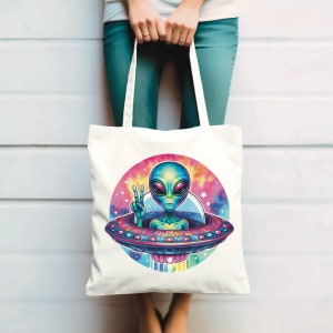 Puede incluir: Bolsa de tela blanca con un gr&aacute;fico colorido de un extraterrestre con piel verde y ojos grandes, haciendo un signo de paz, sentado en un platillo volante sobre un fondo de galaxia.