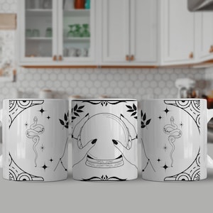 Peut inclure: Trois tasses en céramique blanche avec des illustrations en noir et blanc. La tasse du milieu représente une main tenant une boule de cristal, tandis que les tasses de chaque côté représentent un serpent avec des étoiles.