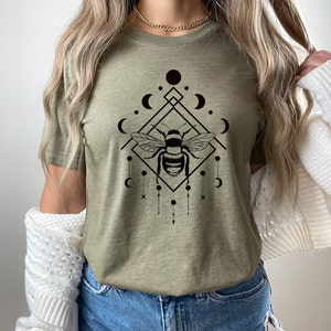 May include: A green t-shirt featuring a black graphic of a bee within a geometric design with moons and stars.