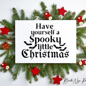 K&ouml;nnte beinhalten: Ein wei&szlig;es bedruckbares Schild mit schwarzem Text, der "Have yourself a Spooky little Christmas" lautet, mit Flederm&auml;usen um das Wort "little". Das Schild ist von gr&uuml;nen Kiefern&auml;sten und roten Sternenschmuck umgeben.