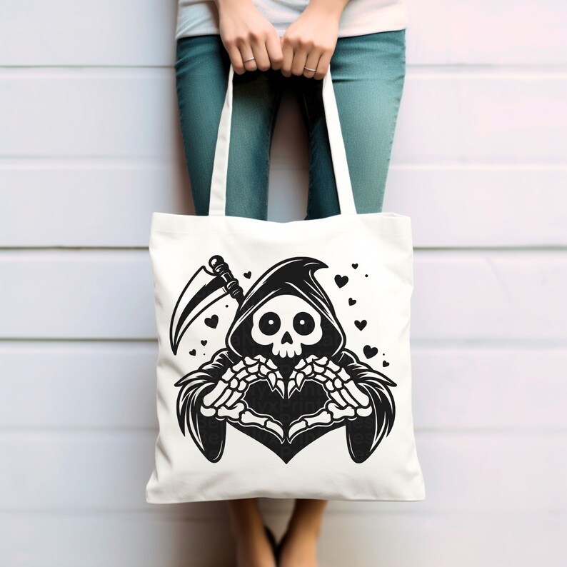 May include: A white tote bag with a black and white illustration of the Grim Reaper making a heart shape with its skeletal hands. The Reaper is wearing a hooded robe and holding a scythe. There are small black hearts scattered around the Reaper.