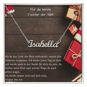 Peut inclure: Un collier argenté avec le prénom "Isabella" écrit en cursive. Il est présenté sur un fond en bois avec du texte en allemand et des boîtes cadeaux. Le texte dit "Für die liebste Tochter der Welt."