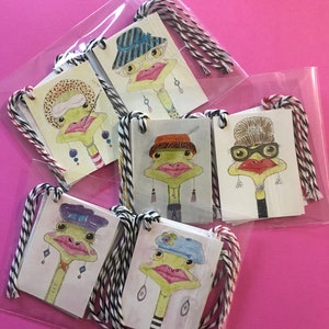 May include: Six colorful gift tags featuring illustrations of ostriches wearing hats and earrings. The tags are packaged in a clear plastic bag with string.