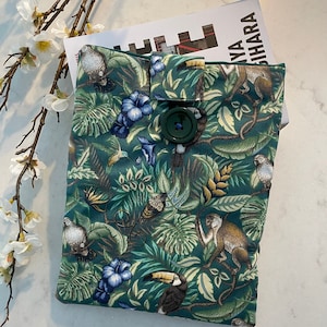 Può includere: Una copertina per libro verde con una stampa di giungla tropicale con tucani, scimmie e pappagalli. La copertina ha una chiusura a bottone.