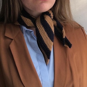 May include: A brown blazer with a blue and brown striped knitted scarf tied around the neck.