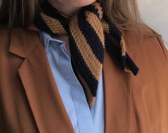 May include: A brown blazer with a blue and brown striped knitted scarf tied around the neck.