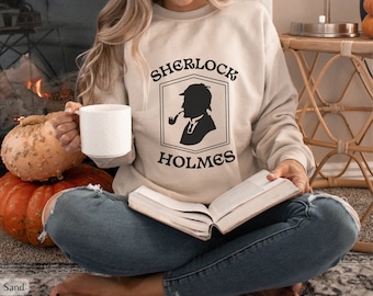 May include: A beige sweatshirt with a black graphic of Sherlock Holmes, featuring the text "Sherlock Holmes" in black.