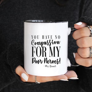 May include: White ceramic coffee mug with a black rim and handle. The mug has black text that reads "You have no compassion for my poor nerves! - Mrs. Bennet"