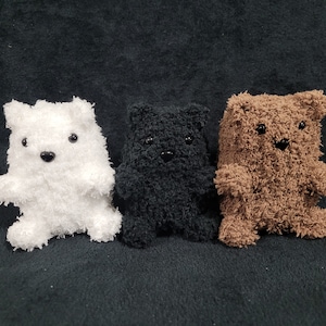 May include: Three plush teddy bears in different colors: white, black, and brown. The bears have black eyes and are made of soft, fuzzy fabric.