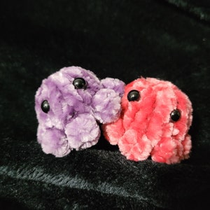 May include: Two small plush octopus toys, one purple and one pink, with black button eyes.