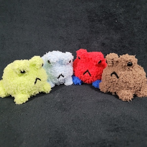 May include: Four plush frog toys in different colors: green, blue, red, and brown. Each frog has a grumpy expression and is made of a soft, fuzzy material.