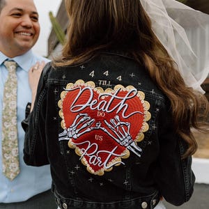 Puede incluir: Chaqueta vaquera negra con un gran diseño de corazón bordado. El corazón presenta las palabras "Death Do Us Part" y manos de esqueleto. La chaqueta tiene cierre de botones, un regalo único para bodas o aniversarios.