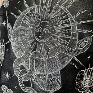 Faux leather jacket featuring stunning metallic silver embroidery in a celestial design. Intricate embroidery showcases a cosmic sun, snake, moon and celestial stars, creating a bold statement jacket for astrology and celestial lovers. Custom made to order with optional colour changes, offering a unique, magical embroidered outerwear piece that stands out from the crowd.