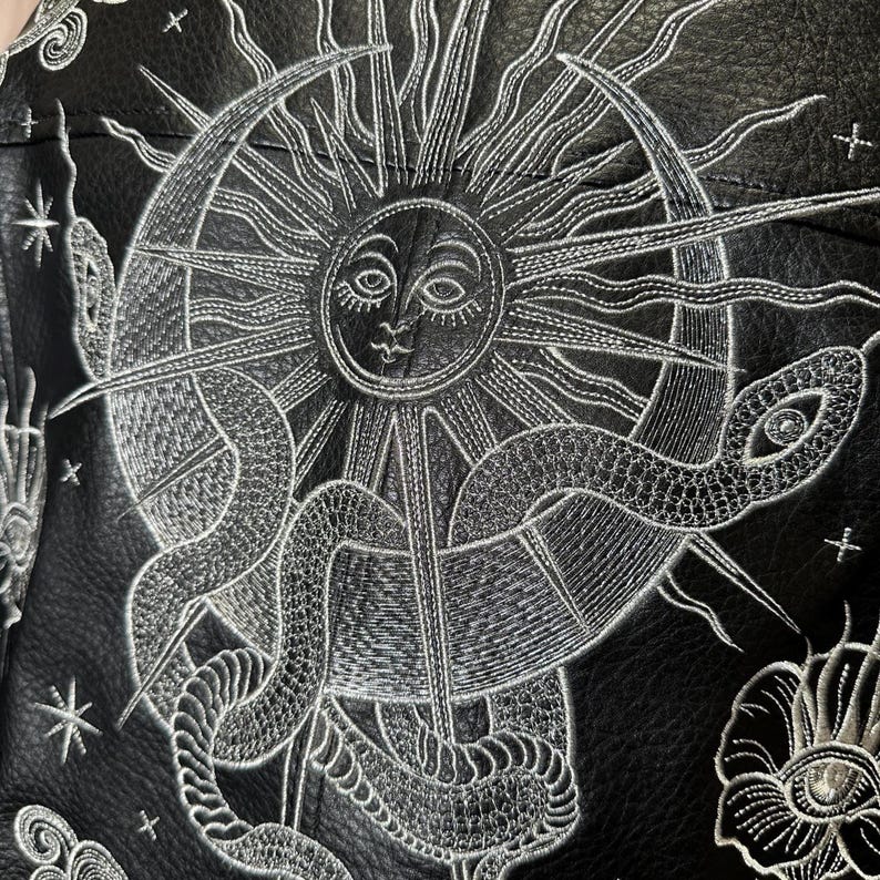Faux leather jacket featuring stunning metallic silver embroidery in a celestial design. Intricate embroidery showcases a cosmic sun, snake, moon and celestial stars, creating a bold statement jacket for astrology and celestial lovers. Custom made to order with optional colour changes, offering a unique, magical embroidered outerwear piece that stands out from the crowd.