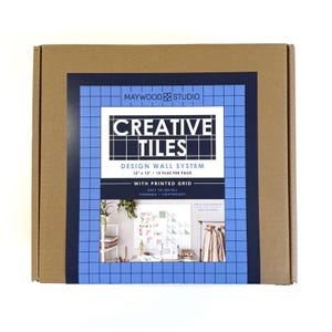 May include: A cardboard box with a blue and white label. The label reads "CREATIVE TILES DESIGN WALL SYSTEM" and includes the text "12 x 12 - 12 TILES PER PACK". The box also states "WITH PRINTED GRID" and "EASY TO INSTALL, PINNABLE, LIGHTWEIGHT".