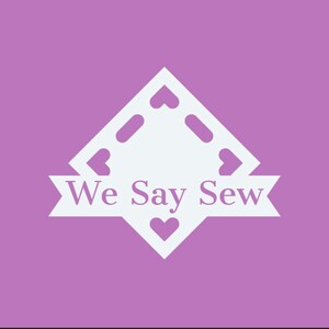 May include: A white logo on a purple background. The logo is a diamond shape with heart cutouts and the words "We Say Sew" in a banner across the bottom. The background is a solid, light purple color.