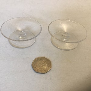 May include: Two clear glass pedestal dishes with a scalloped edge. The dishes are approximately 2 inches in diameter.