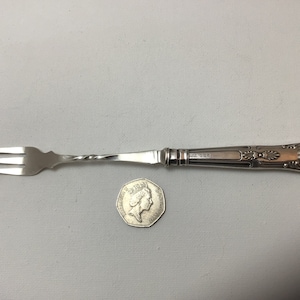 May include: A silver cake fork with a twisted handle and an ornate design. The fork has three tines and is approximately 18 cm long.