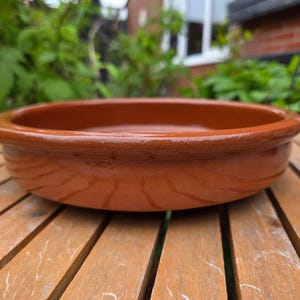 May include: A terracotta serving dish with a rounded rim. The dish is glazed and has a light brown colour.