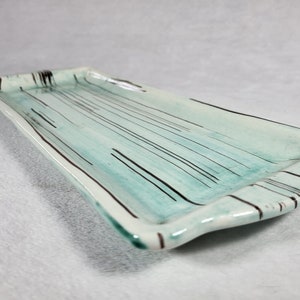 May include: A rectangular ceramic serving tray with a light blue glaze and black stripes. The tray has a slightly curved edge.
