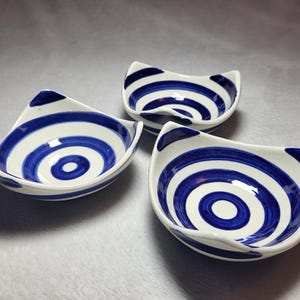 May include: Three white ceramic bowls with blue and white concentric circle designs. The bowls are slightly angled and have a wavy edge.