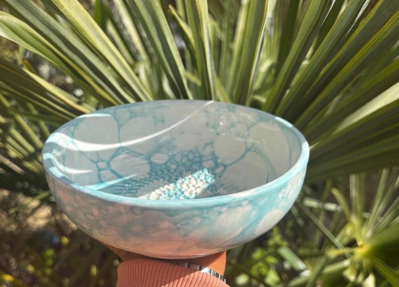 Puede incluir: Un cuenco de cer&aacute;mica redondo con una base blanca y un patr&oacute;n de burbujas de color azul claro en las superficies interior y exterior. El cuenco tiene un acabado liso y brillante con una forma circular constante y un borde curvado.