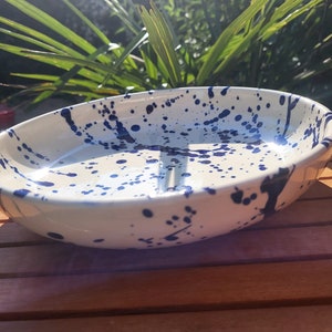 May include: A white ceramic serving dish with a blue splatter design. The dish is oval shaped and has a slightly raised rim.