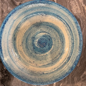 May include: A large, white ceramic bowl with a blue and white swirl design. The bowl has a speckled glaze and a wide, shallow shape.