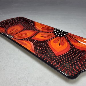 May include: A rectangular ceramic serving dish with a black background and a red and orange floral design. The dish is decorated with small black dots.