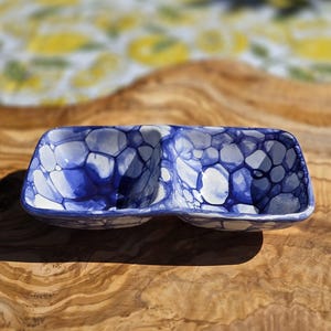 May include: A rectangular, divided serving dish with a blue and white abstract pattern. The ceramic dish sits on a wooden surface. The design features a network of blue shapes against a white background.