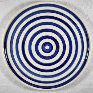 May include: A white ceramic plate with a blue concentric circle design.