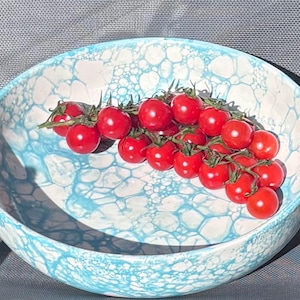 May include: A ceramic bowl with a blue and white bubble pattern holds a cluster of bright red cherry tomatoes. The tomatoes are on green stems. The bowl is round and has a wide rim.