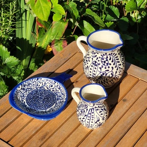 May include: Three ceramic kitchenware items with blue and white floral patterns. A small pitcher, a larger pitcher, and a small dish with a handle.