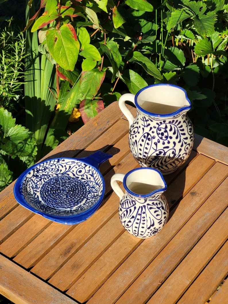 May include: Three ceramic kitchenware items with blue and white floral patterns. A small pitcher, a larger pitcher, and a small dish with a handle.