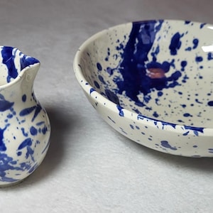 May include: A white ceramic pitcher and bowl with a blue and white splatter paint design.