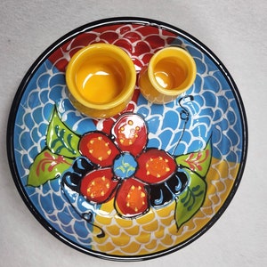 May include: A colourful ceramic serving dish with a blue, yellow and red floral design. The dish has two small yellow bowls on top.