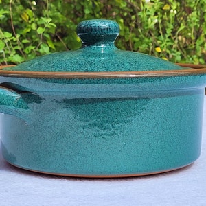 May include: A teal blue ceramic casserole dish with a lid and two handles. The dish has a speckled glaze and a brown rim.