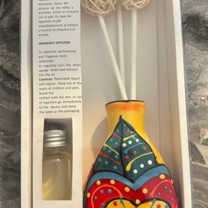 May include: A ceramic diffuser vase with a colourful floral design. The vase is filled with three white sticks and a small bottle of oil. The packaging includes instructions for use and safety precautions.