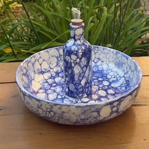 May include: A ceramic serving bowl with a central integrated bottle, featuring a blue and white bubble-like pattern throughout. The bottle is topped with a cork stopper and a clear glass pourer, creating a cohesive set for serving liquids.