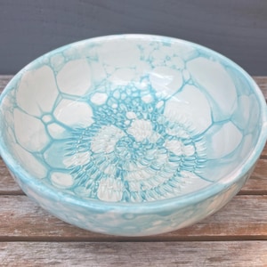 May include: A ceramic bowl with a light blue and white pattern. The bowl's interior features a spiral design in shades of blue and white. The bowl is round and sits on a wooden surface.