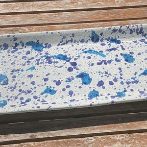 May include: A rectangular serving tray with rounded corners, featuring a white base colour decorated with a speckled pattern of vibrant blue and purple paint splatters across the entire surface, creating a distinct and colourful visual effect.